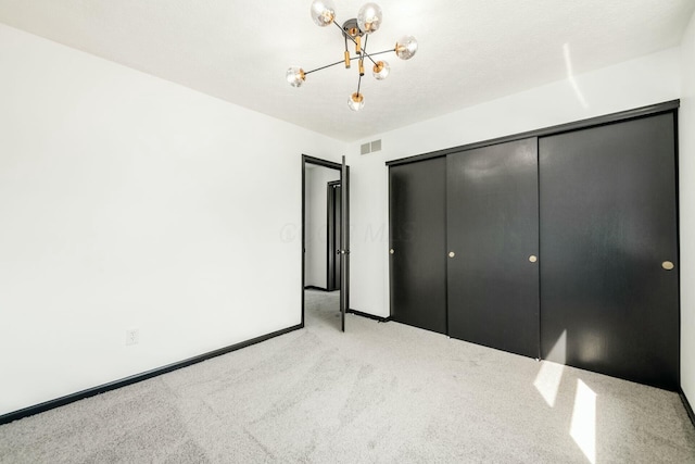 unfurnished bedroom with carpet flooring, visible vents, a closet, baseboards, and a notable chandelier