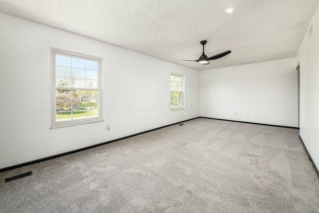 carpeted empty room with a textured ceiling, visible vents, ceiling fan, and baseboards