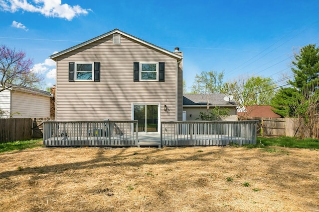 back of property featuring a lawn, a chimney, a deck, and a fenced backyard