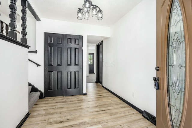 foyer with wood finished floors, baseboards, a notable chandelier, and stairs