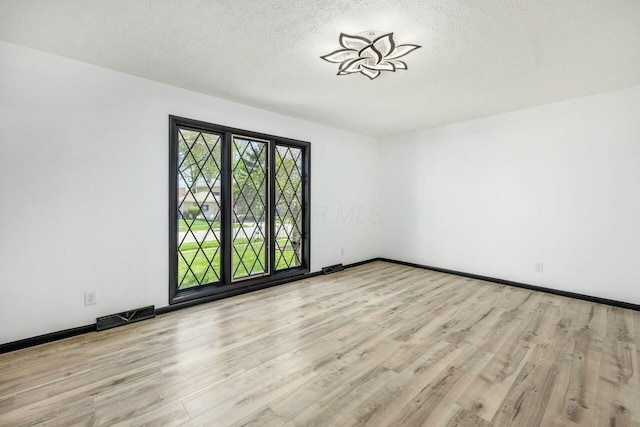 empty room with a textured ceiling, visible vents, wood finished floors, and baseboards