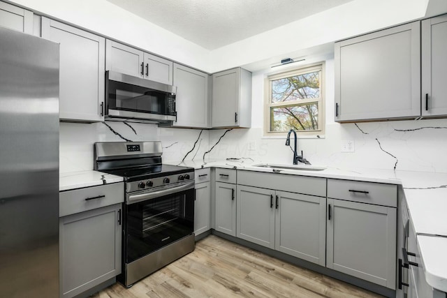 kitchen featuring tasteful backsplash, light wood-style flooring, stainless steel appliances, a sink, and gray cabinetry