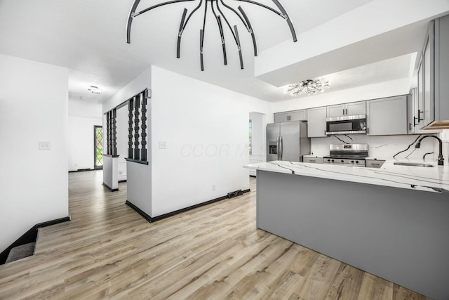 kitchen featuring gray cabinetry, light wood finished floors, a sink, and appliances with stainless steel finishes