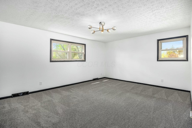 empty room with a textured ceiling, an inviting chandelier, carpet, and baseboards