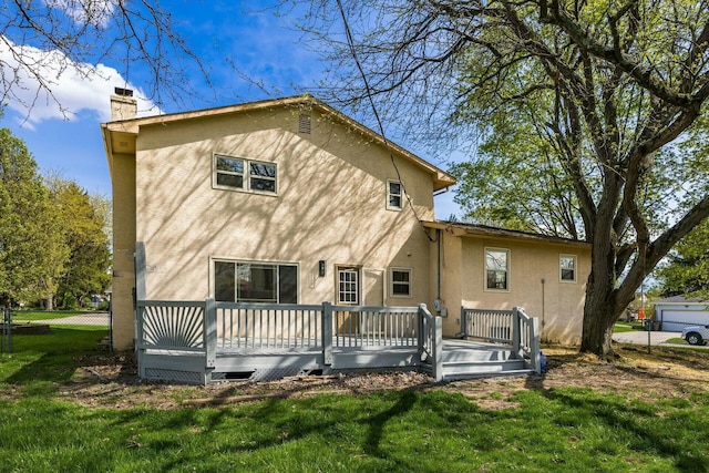 rear view of house featuring stucco siding, fence, a chimney, and a lawn
