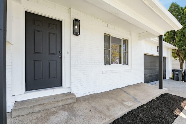 entrance to property featuring covered porch, brick siding, and a garage