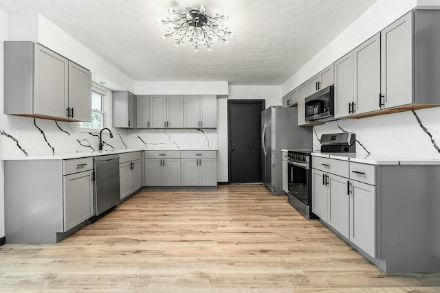 kitchen with gray cabinets, appliances with stainless steel finishes, light countertops, backsplash, and light wood finished floors