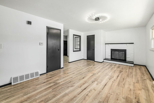 unfurnished living room featuring baseboards, visible vents, wood finished floors, and a glass covered fireplace