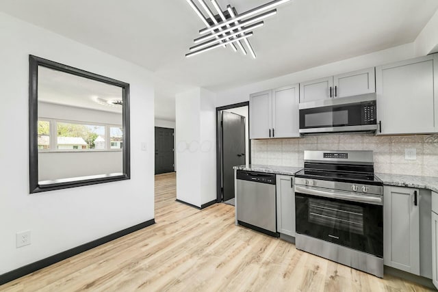kitchen with appliances with stainless steel finishes, tasteful backsplash, light stone countertops, and gray cabinets