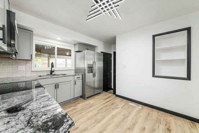 kitchen featuring gray cabinetry, a sink, light stone counters, and stainless steel fridge with ice dispenser