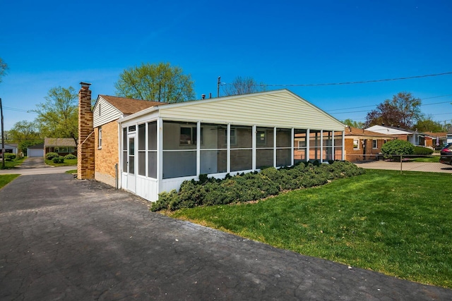 view of property exterior with a chimney, roof with shingles, a sunroom, and a lawn