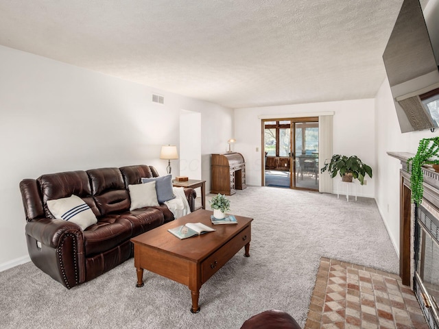 living room featuring carpet floors, a glass covered fireplace, a textured ceiling, and visible vents