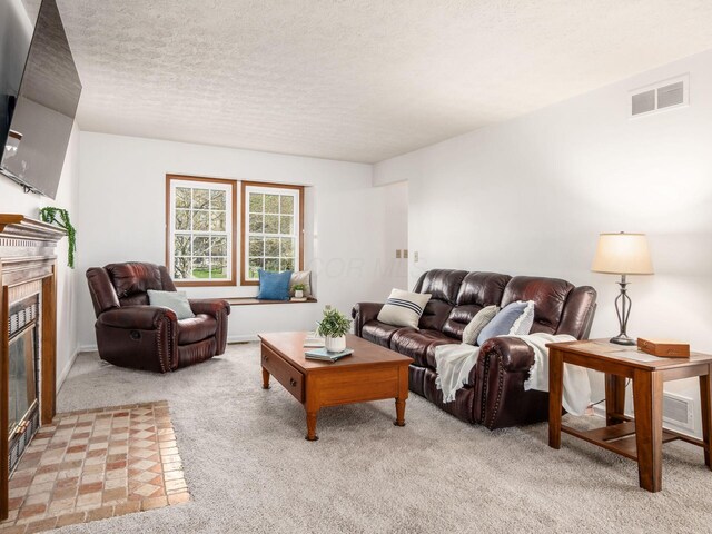 living area with visible vents, light carpet, baseboards, a glass covered fireplace, and a textured ceiling