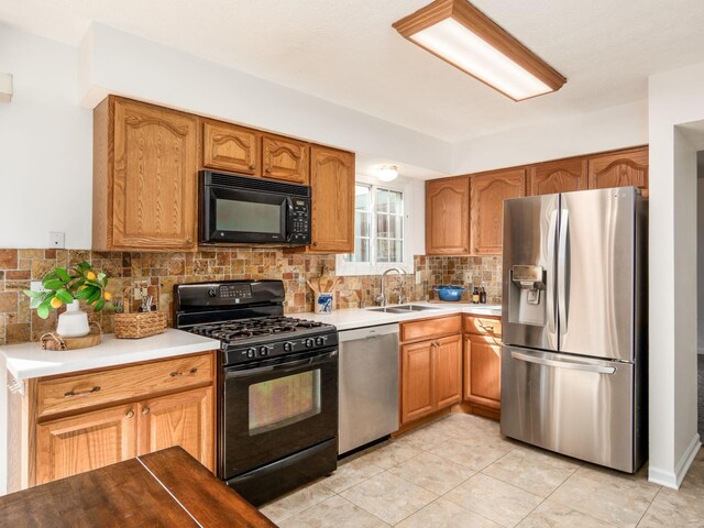 kitchen featuring a sink, brown cabinetry, black appliances, light countertops, and backsplash