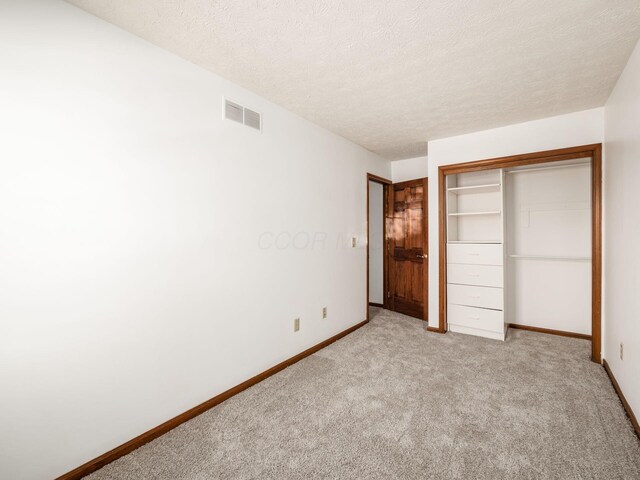 unfurnished bedroom with light carpet, a textured ceiling, baseboards, visible vents, and a closet