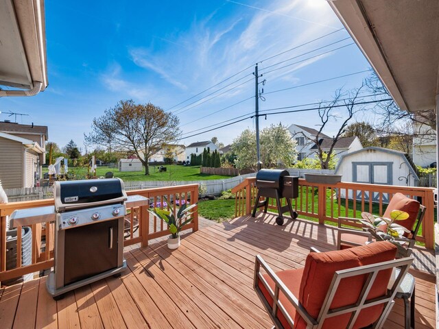 wooden deck with area for grilling, a fenced backyard, a shed, an outbuilding, and a lawn