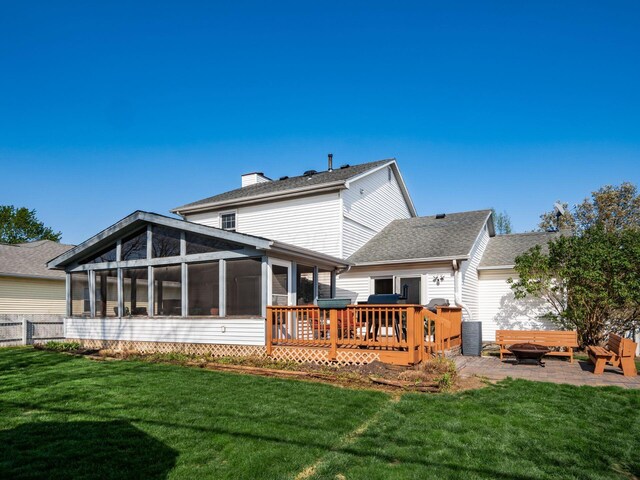 rear view of property featuring a chimney, a deck, an outdoor fire pit, a yard, and a sunroom