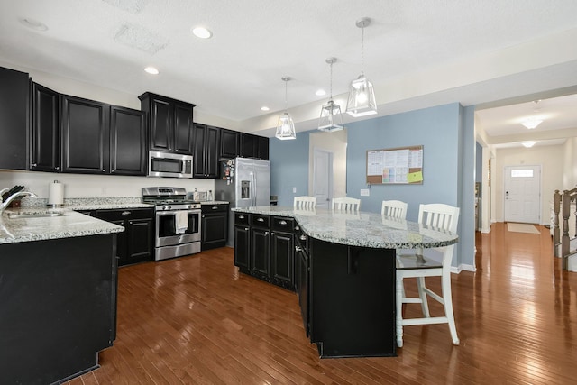 kitchen featuring dark cabinets, stainless steel appliances, a kitchen island, and a sink