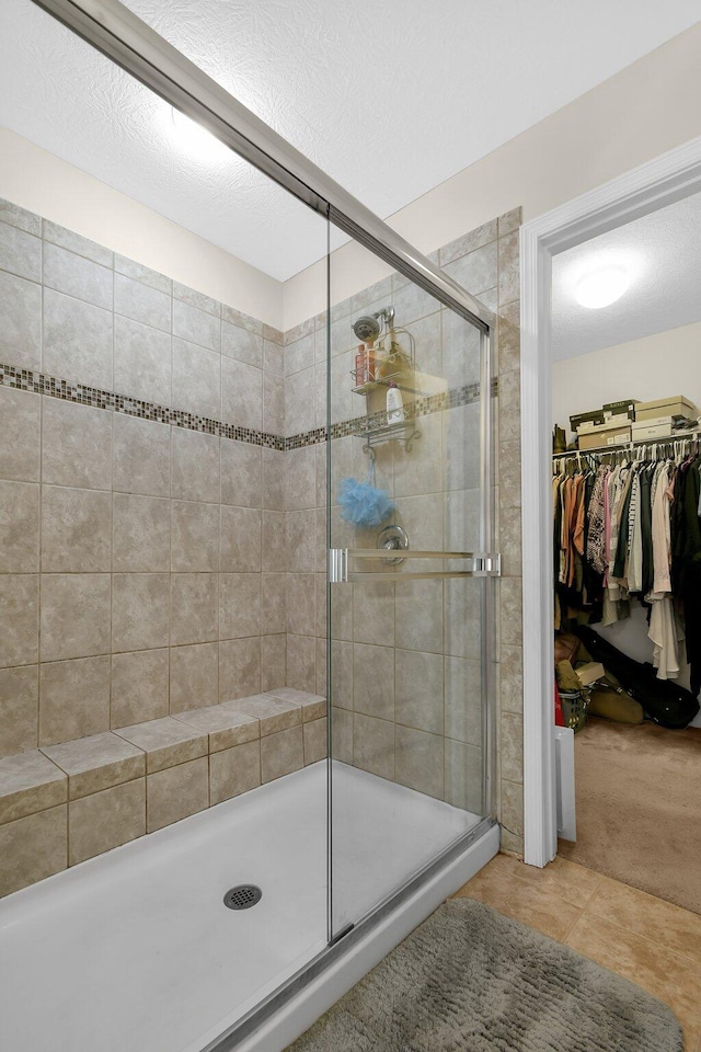 bathroom featuring tile patterned floors, a textured ceiling, a walk in closet, and a stall shower