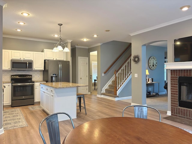 33 Hampden Dr, Granville, OH 43023 - kitchen featuring appliances with stainless steel finishes, a fireplace, light wood finished floors, a kitchen island, and tasteful backsplash