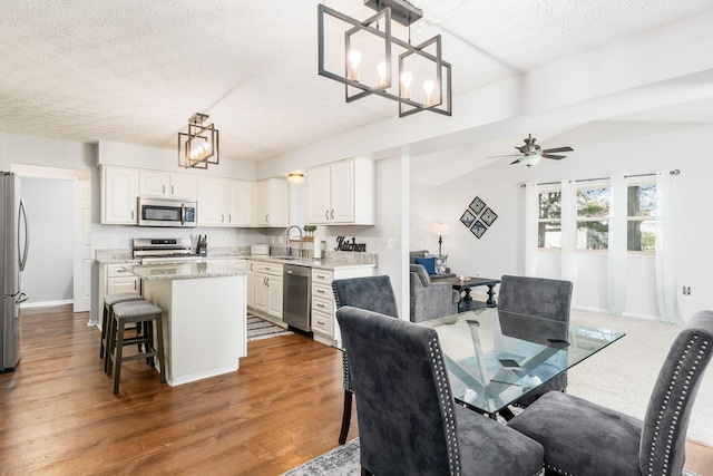 dining area featuring wood finished floors, a textured ceiling, baseboards, and ceiling fan with notable chandelier