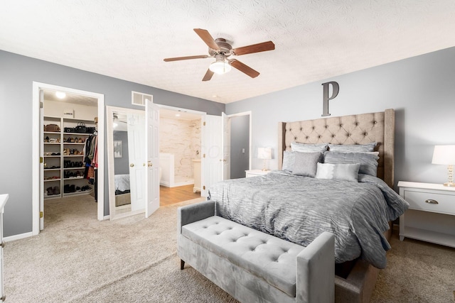 bedroom with a textured ceiling, a closet, a walk in closet, carpet floors, and visible vents