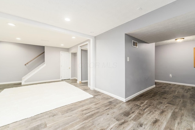 finished below grade area featuring wood finished floors, visible vents, baseboards, and stairs