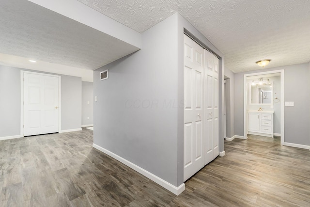hallway featuring baseboards, wood finished floors, visible vents, and a textured ceiling