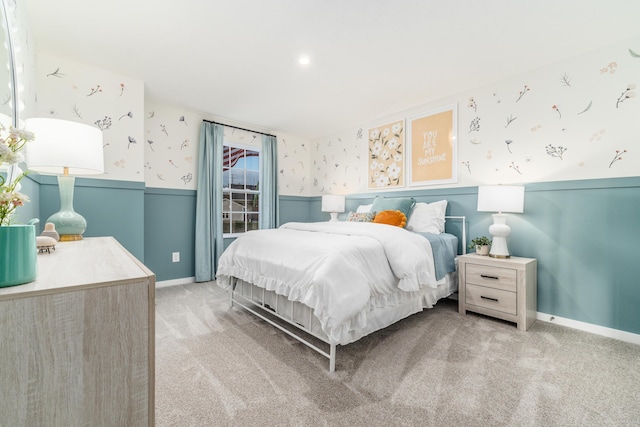 bedroom featuring wallpapered walls, wainscoting, light carpet, and baseboards