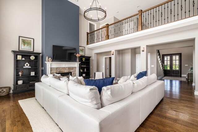 living room featuring a towering ceiling, wood finished floors, a fireplace, baseboards, and a chandelier