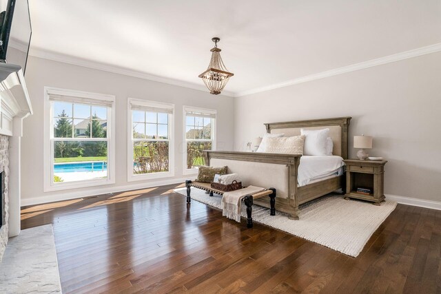 bedroom with a stone fireplace, hardwood / wood-style floors, a chandelier, baseboards, and ornamental molding