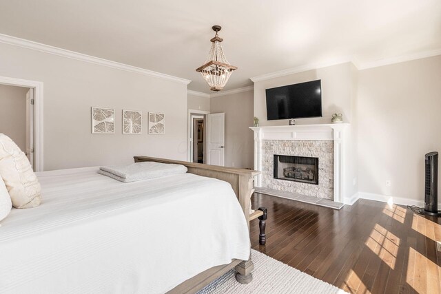 bedroom with a chandelier, dark wood finished floors, crown molding, baseboards, and a fireplace