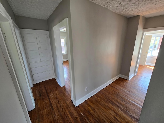 hall featuring dark wood finished floors, a textured ceiling, and baseboards