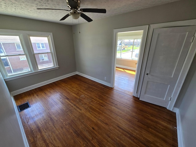 empty room featuring dark wood finished floors, baseboards, ceiling fan, and visible vents