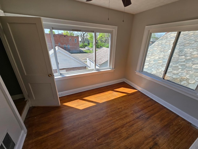 empty room with baseboards, visible vents, dark wood-style floors, and ceiling fan