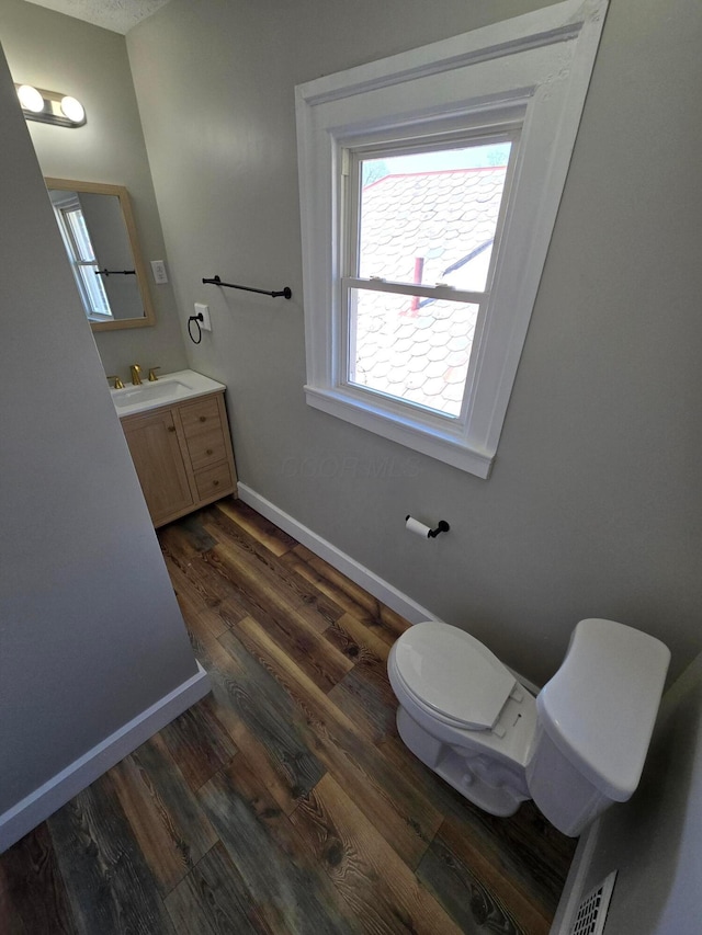 half bath featuring toilet, vanity, wood finished floors, and baseboards