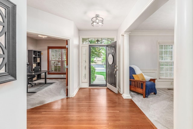 entryway featuring crown molding, wood finished floors, baseboards, ornate columns, and carpet