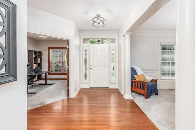 entrance foyer with crown molding, light colored carpet, light wood-style flooring, baseboards, and decorative columns