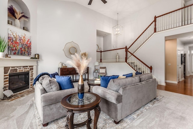 living area featuring a ceiling fan, a stone fireplace, stairway, high vaulted ceiling, and carpet