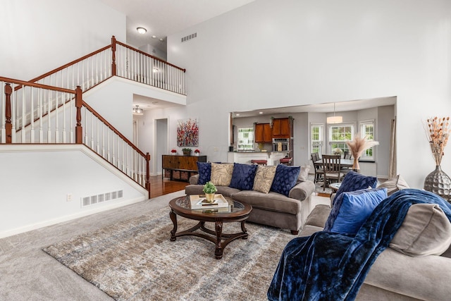 carpeted living room with a high ceiling, visible vents, and stairway