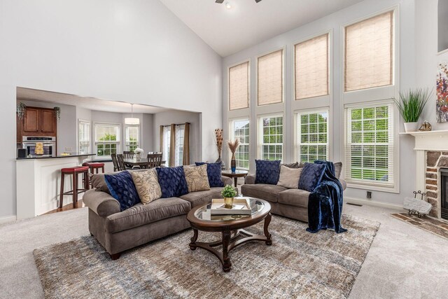 living area featuring high vaulted ceiling, ceiling fan, carpet, and a stone fireplace