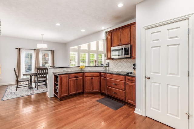 kitchen with brown cabinets, stainless steel microwave, light wood-style flooring, and tasteful backsplash