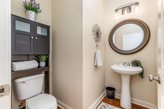 half bathroom with a sink, baseboards, toilet, and wood finished floors