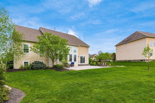 rear view of house with a shingled roof, a patio, stucco siding, and a yard