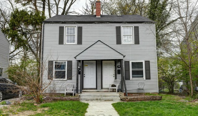colonial-style house featuring a chimney, a front lawn, fence, and a shingled roof