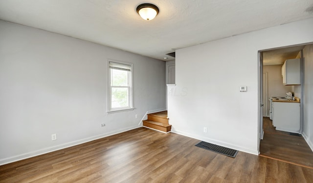 empty room featuring baseboards, wood finished floors, visible vents, and stairs