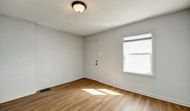 unfurnished room featuring visible vents, wood finished floors, baseboards, and a healthy amount of sunlight