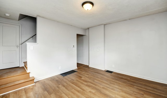 unfurnished living room with baseboards, light wood-style flooring, visible vents, and stairs