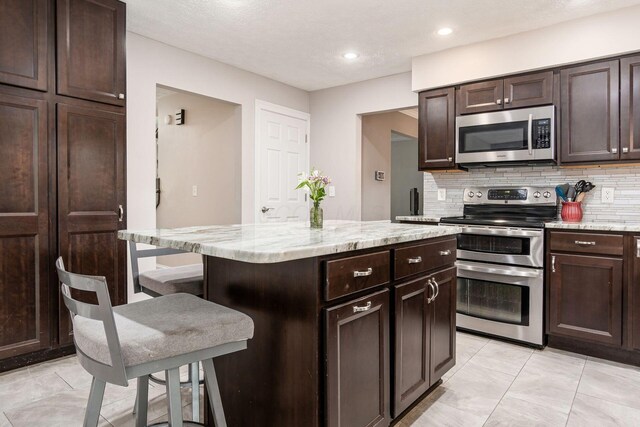 1123 Firth Ave, Worthington, OH 43085 - kitchen with stainless steel appliances, tasteful backsplash, a center island, a kitchen bar, and dark brown cabinetry
