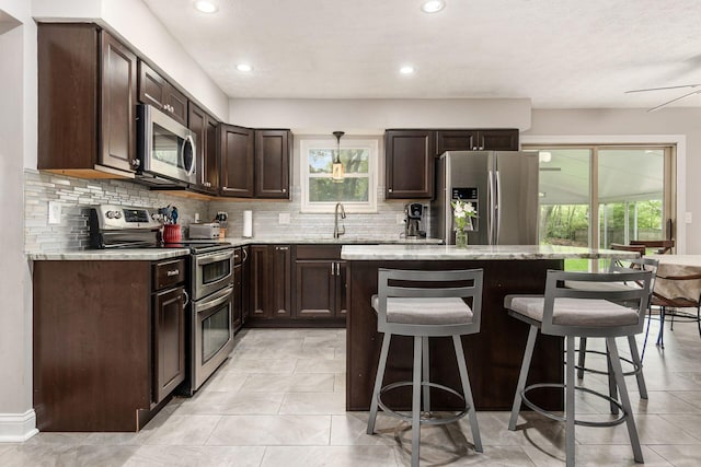 1123 Firth Ave, Worthington, OH 43085 - kitchen featuring appliances with stainless steel finishes, a kitchen bar, tasteful backsplash, dark brown cabinets, and healthy amount of natural light